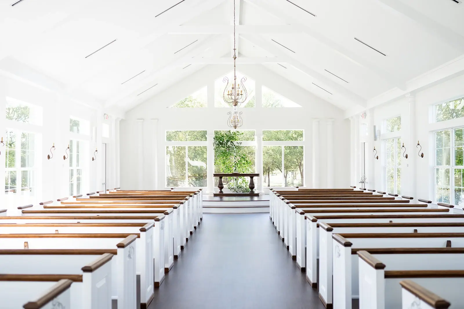 The actual chapel with white pews and warm wood tops, vaulted white ceiling and glazed altar wall